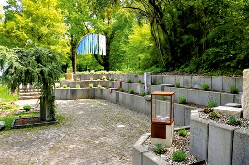 Im Pflasterbelag sind die Tierkreiszeichen als Juraplatten eingelassen. Im Vordergrund rechts die Laterne mit Kerzenfach als Symbol für Feuer sowie hinten die blaue Fahne für das Element Luft.